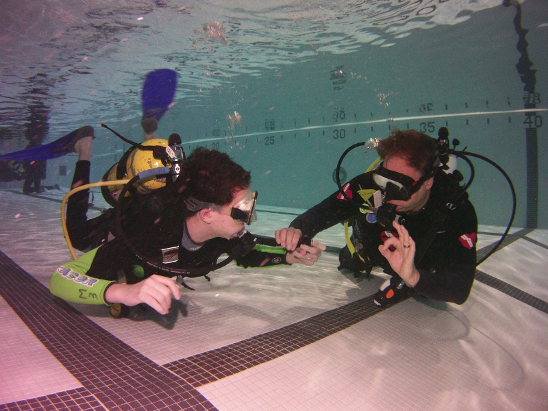 Young adaptive diver and dive buddy using underwater hand signals in a pool